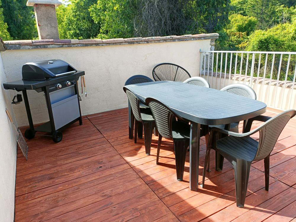 Terrasse privée de l'appartement Le Romane à Vallon Pont d'Arc avec table extérieure, barbecue à gaz et vue sur le vieux Vallon et la végétation en Ardèche
